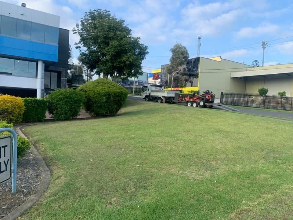 Maintained lawns and shaped shrubs outside commercial premises, with grounds maintenance equipment on site